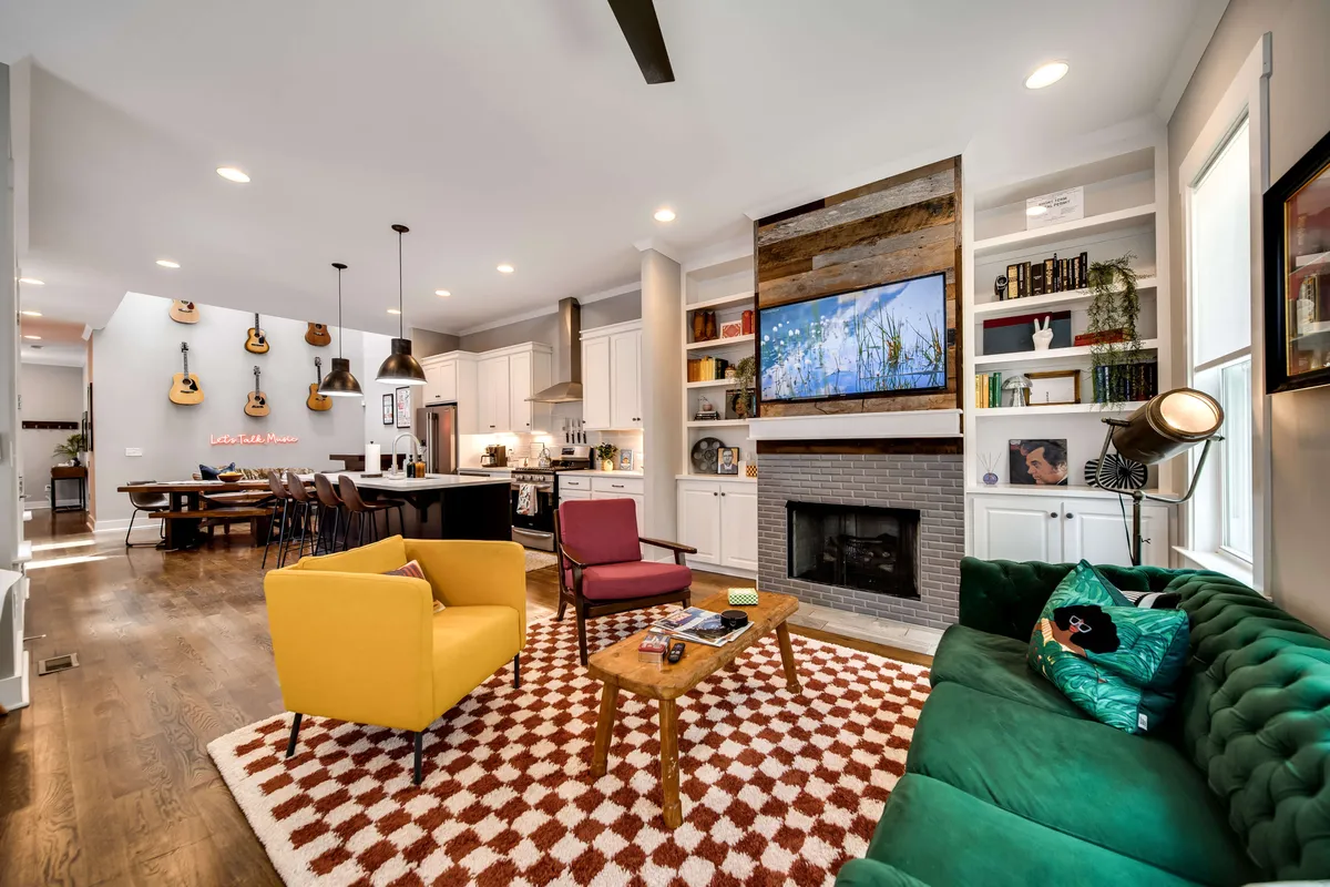 A welcoming living area with a green sofa, yellow chair, wooden coffee table, fireplace, and shelves filled with decor. The seating is arranged for easy conversation and relaxation, and the overall mood is comfortable yet elevated.