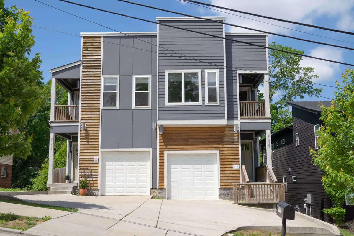 A contemporary exterior shot of the property showing its modern architectural design, featuring wood and gray siding, large windows, and inviting garage doors. The spacious front porch hints at communal outdoor gatherings and relaxation.